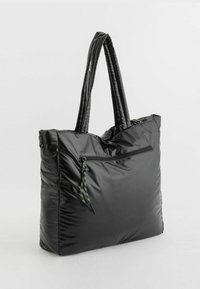 Czarna, wypchana torba na ramię z błyszczącego materiału; posiada dwa długie uchwyty oraz przednią kieszeń na zamek z kolorowym sznurkiem do ściągania.