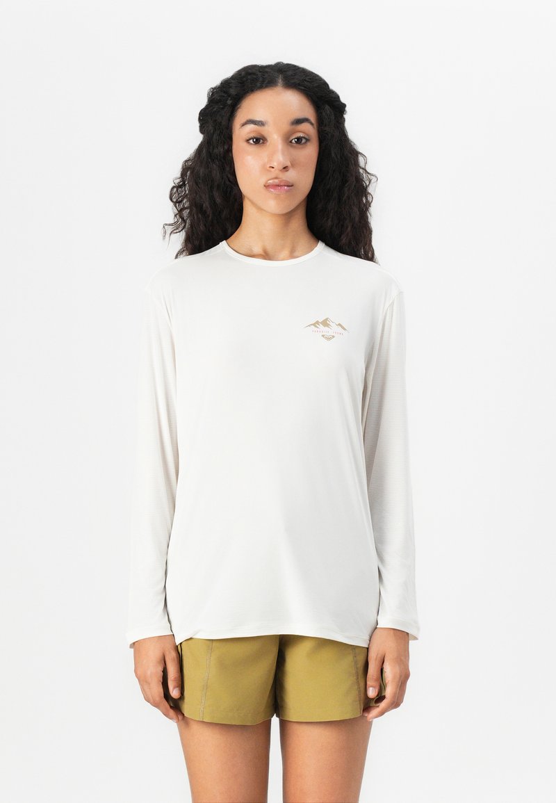 Leichte langärmelige Bluse in Creme mit einem kleinen bergegrafischen Motiv in Gold, kombiniert mit olivgrünen Shorts. Glatte Textur und entspannte Passform.