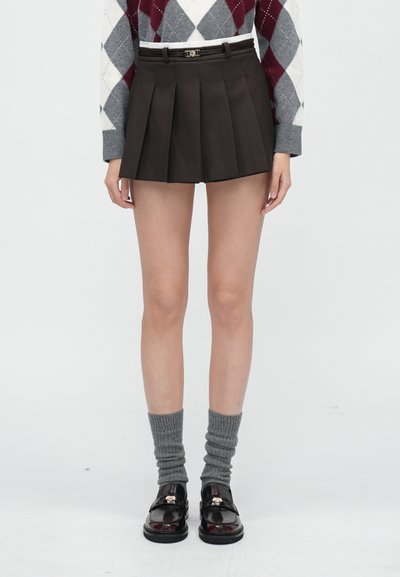 Čierna plisovaná sukňa s pásom, kombinovaná so sivými rebrovanými ponožkami a lesklými čiernymi mokasínami. Hladká tkanina so štruktúrovaným dizajnom.