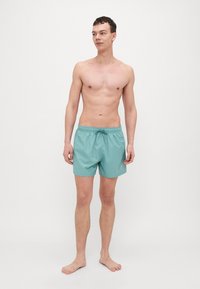 Turkoosi uimashortsit, jotka on valmistettu kevyestä materiaalista. Niissä on joustava vyötärö, jossa on nyöri, sekä minimalistinen logotulos.