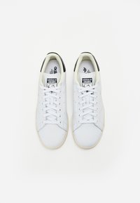 Hvide lædersneakers med perforerede detaljer, flade snørebånd, en sort accent på hælen, og en tekstureret gummisål.