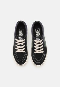 Black canvas sneakers with white laces, contrasting green side accents, and a textured grey heel. Features white stitching and logo on the tongue.