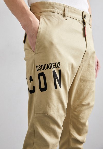 Pantaloni cargo in cotone beige con una superficie liscia, grande stampa nera "ICON", tasche laterali e chiusura zip con un piccolo tag di marca.