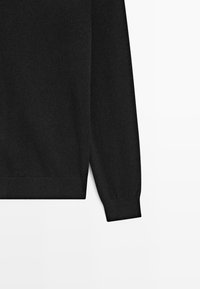 Maglione nero a maniche lunghe, con polsini e orlo a costine, realizzato in un morbido tessuto a maglia. Texture liscia senza motivi o dettagli visibili.