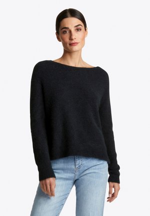 Un pull en tricot noir avec un large col, des manches longues et des poignets côtelés, associé à un jean bleu clair. La texture semble douce et confortable.