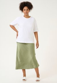 T-shirt en coton blanc à manches courtes associé à une longue jupe en satin olive. L'ensemble présente des lignes simples et une coupe décontractée.