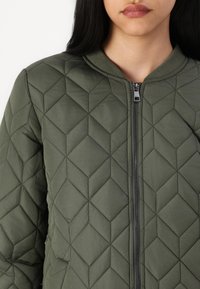 Prešívaná zelená bomber bunda s diamantovým vzorom, so zipsom vpredu a rebrovaným golierom. Hladká textúra a ľahký materiál.