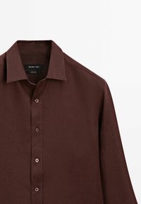Chemise en lin marron foncé à manches longues avec col et quatre boutons visibles, présentée sur fond blanc.