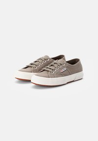 Et par beige lavtopps kanvas sneakers med hvite gummisåler og snørebånd, vist mot en enkel hvit bakgrunn.