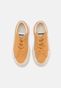 Keltaiset kanvaakenkäet, pyöreällä kärjellä, valkoisella kumipohjalla ja vastaavilla nauhoilla. Sisältää "Converse All Star" -logon kielessä.