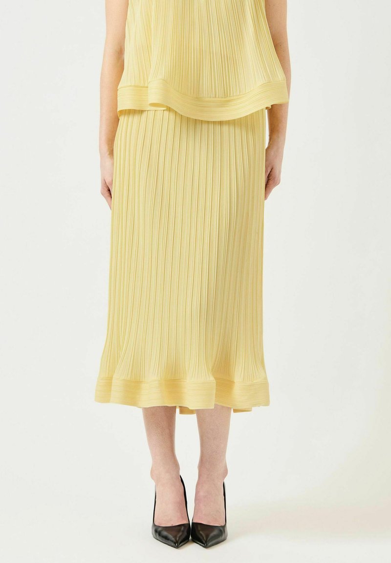 Conjunto de dos piezas plisado en tejido amarillo suave; incluye un top sin mangas y una falda midi con textura lisa y dobladillo en capas.