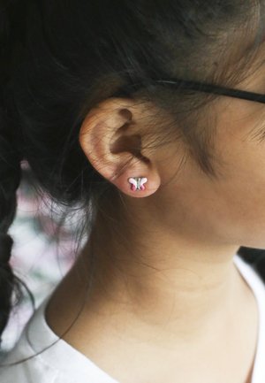 Vlindervormige oorbellen in zilver met roze en witte accenten, met een metallic afwerking en een zachte textuur, gedragen aan een oor.