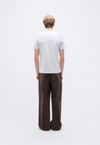 Ανοιχτό γκρι μπλουζάκι με κοντά μανίκια, συνδυασμένο με άνετο, σκούρο καφέ, φαρδύ παντελόνι. Απλός σχεδιασμός, λεία υφή, χωρίς εμφανή μοτίβα ή λογότυπα.