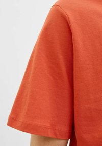 Kortærmet T-shirt i livlig orange bomuld, med rund halsudskæring, glat tekstur og ren syning langs kanten.