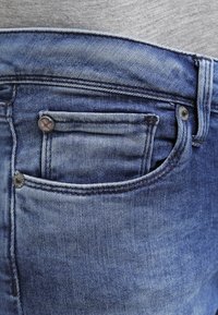 Blue denim jeans with a classic five-pocket design, featuring a front pocket and metal hardware accents. Smooth texture and faded finish.