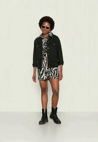 Jaqueta de ganga preta curta sobre um vestido camiseiro com estampa de zebra em preto e branco. A modelo usa óculos de sol redondos e botas de combate pretas com atacadores.