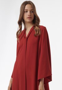 Rood, lichtgewicht, lang mouwgedragen kledingstuk met een V-hals en een vloeiende silhout. De stof heeft een zachte textuur en subtiele drape.
