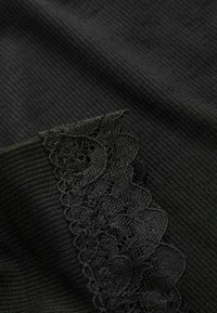 Schwarzer gerippter Stoff mit einem gewellten schwarzen Spitzenrand am Rand, der der Gesamtdesign Textur und Detail verleiht.