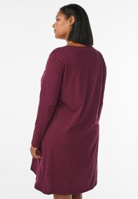 Abito bordeaux a maniche lunghe con vestibilità rilassata, scollatura rotonda e lunghezza a metà coscia. Tessuto morbido con una consistenza liscia e senza motivi visibili.