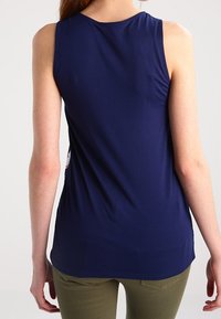 Top senza maniche blu navy con una texture liscia, scollatura rotonda e orlo curvato. La vista posteriore mostra una silhouette aderente.