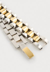 Zilveren en goudkleurige metalen horlogeband met in elkaar grijpende schakels; heeft gepolijste en geborstelde afwerkingen, een lichte kromming en een sluitmechanisme.