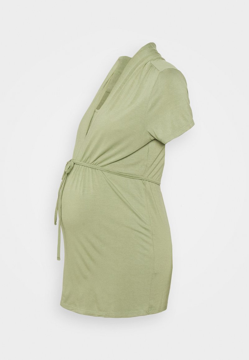 Vestido de maternidade em verde claro, com mangas curtas, design cruzado com um laço na cintura, tecido suave, destacando a forma arredondada da barriga.