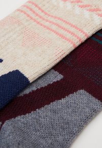 Due paia di calze di lana: una crema con motivi rosa e blu, l'altra bordeaux con disegni geometrici grigi e blu teal, tessuto a maglia texturata.
