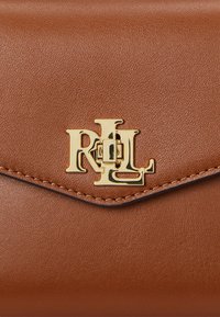 Brun läderplånbok med en strukturerad yta, med en logotyp i guldton och en sömnadsdetalj i kanten.