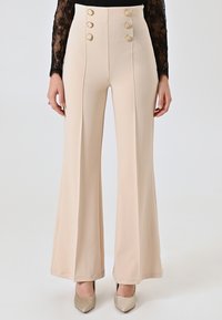 Beige high-waisted broek van een soepele stof met uitlopende pijpen, voorzien van vier goudkleurige knoopsaccenten aan de voorkant en verticale naden.