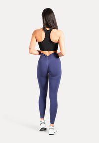 Débardeur de sport noir court et leggings bleu marine avec un détail de couture unique dans le dos, associés à des baskets blanches avec des accents métalliques.