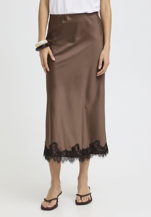 Bruine satijnen midi-rok met zwarte kanten rand, gecombineerd met een wit topje, zwart-witte armbanden en donkerbruine sandalen.