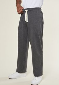 Graue Sweatpants aus weichem Stoff, mit einem elastischen Bund, seitlichen Taschen und einer lockeren Passform. Kombiniert mit weißen Turnschuhen.