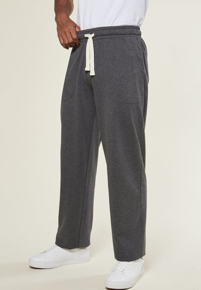 Graue Sweatpants aus weichem Stoff, mit einem elastischen Bund, seitlichen Taschen und einer lockeren Passform. Kombiniert mit weißen Turnschuhen.