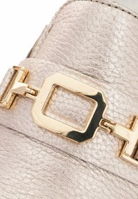 Metalen zilveren leren schoen met een opvallende gouden rechthoekige gespdetails, met een gestructureerd oppervlak en gladde randen.