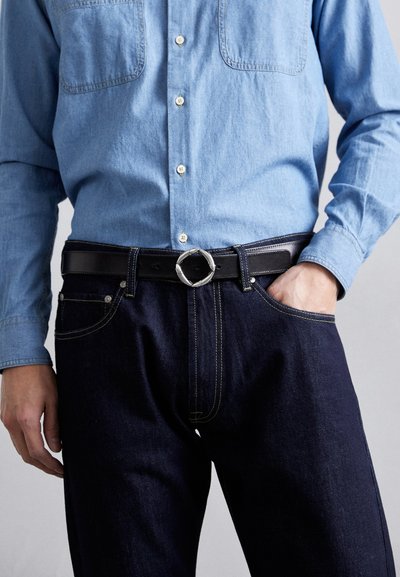 Dark blue denim jeans with yellow stitching, paired with a light blue chambray shirt and a black leather belt featuring a round silver buckle.