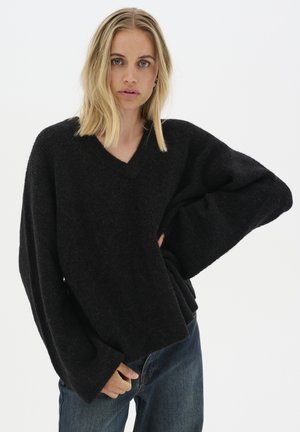 Schwarzer übergroßer Pullover mit V-Ausschnitt, strukturiertem Stoff, weiten Ärmeln und lockerer Passform, kombiniert mit blauen Jeans.