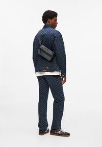 Denim jacket and pants in dark blue houndstooth pattern, paired with a black crossbody bag and black sneakers with brown soles.