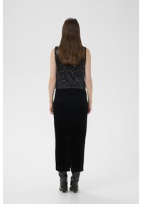 Juodas topas su blizgančiais karoliukais ir be rankovių, derinamas su ilgą juodą aksominę sijoną. Modelis dėvi juodus batai iki kelių.