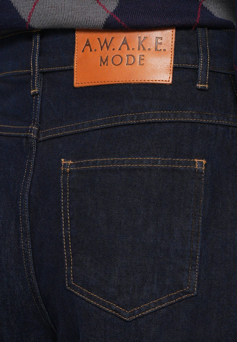 Jeans in denim con una vestibilità a vita media, colore blu scuro, con cuciture arancioni e un'etichetta in pelle beige impressa con "A.W.A.K.E. MODE."