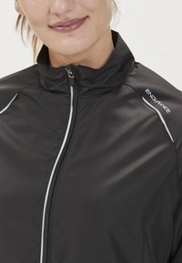 Zwarte zip-up jas met een hoge kraag, witte accentstrepen op de schouders en de merknaam "ENDURANCE" op het rechter schoudergebied.