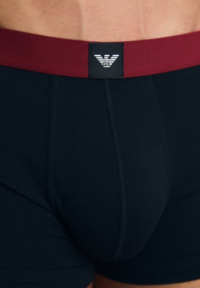 Črne bokserice z maroon elastičnim pasom. Elastični pas vsebuje črn oznako z logotipom. Gladek material z oprijetim dizajnom.