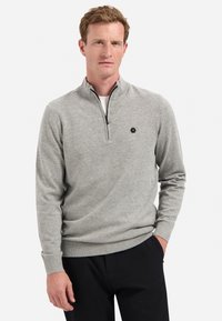 Grauer Pullover mit Reißverschluss und weichem Stoff, der ein tailliertes Design, gerippte Bündchen und ein kleines Sechseck-Logo auf der Brust aufweist.