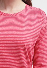 Maglietta a strisce rossa e rosa con una texture leggera e morbida. Caratterizzata da un collo rotondo e maniche corte, con sottili strisce orizzontali.