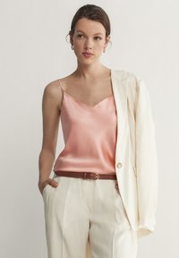 Rosa satin cami med tunna axelband, tillsammans med en vit kavaj och ljusbeiga byxor, accentuerad med ett brunt bälte. Minimalistisk design.