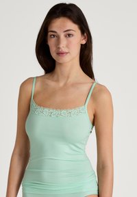 Mint green camisole with adjustable straps, featuring a lace trim along the neckline. Made from soft, smooth fabric with a fitted shape.