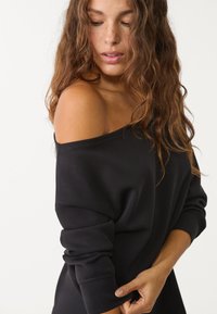 Schwarzer Off-Shoulder-Sweatshirt mit langen, umgeschlagenen Ärmeln. Weiches Material, lockere Passform und sichtbare Nähedetails an den Schultern.