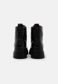 Bottines noires laquées avec un talon épais, des accents de logo et une doublure rouge contrastante. Comprend des languettes pour un enfilage facile.