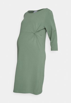 Robe de maternité verte à manches trois-quarts avec un détail froncé sur le côté et un col rond, présentée sur un fond uni.