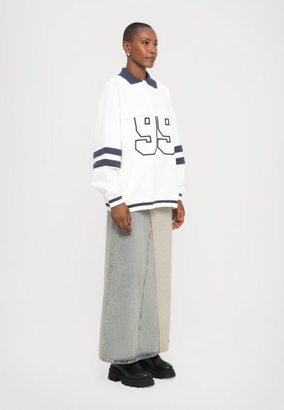 White long-sleeve shirt with navy stripes, number 99, paired with a two-tone, long denim skirt. Black platform boots complete the outfit.