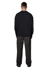 Czarna, długorękawowa koszula o luźnym kroju i opadających ramionach, zestawiona z ciemnymi spodniami cargo z bocznymi kieszeniami.